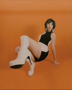 a woman in short shorts and high heels is posing for a photo on an orange background