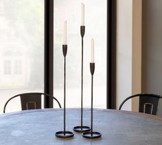 three candles sitting on top of a table next to two black chairs and a window