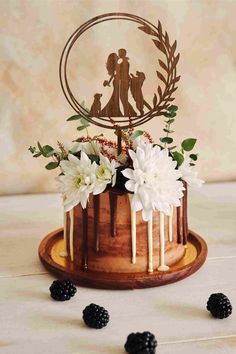 a cake decorated with white flowers and greenery on a wooden platter next to blackberries