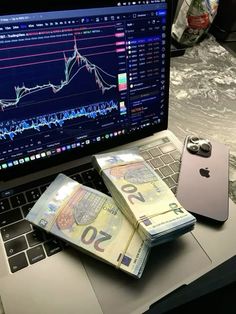 an open laptop computer sitting on top of a desk next to stacks of euro notes