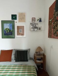 a bed sitting in a bedroom next to a wall with pictures on it and a lamp