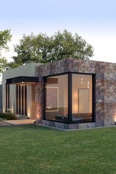 a small modern house in the middle of a grassy area with lights on it's windows