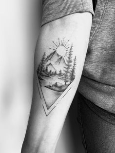 a woman's arm with a mountain and pine trees tattoo on the left forearm