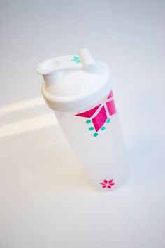 a white cup with pink and green designs on the lid is sitting on a table