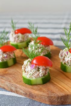 small cucumbers topped with tuna and tomatoes on a wooden cutting board, garnished with fresh dill