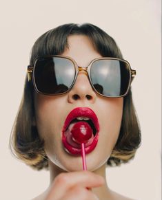 a woman wearing sunglasses and holding a lollipop in front of her face with the tongue out