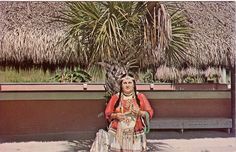 an old photo of a woman sitting on a bench in front of a palm tree