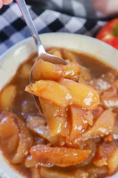 a spoon full of food on top of a white bowl with apples in the background