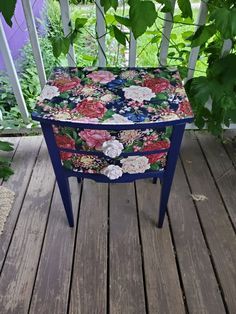 a blue table with flowers on it sitting on a wooden deck next to some plants