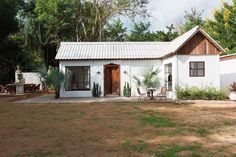 a small white house sitting in the middle of a field with lots of trees around it