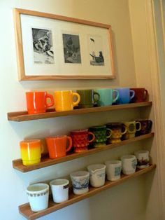 two wooden shelves with cups and mugs on them in front of a framed photograph