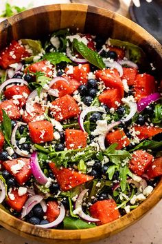 a salad in a wooden bowl with blueberries, onions and feta cheese on top