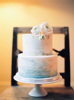 a white and blue wedding cake sitting on top of a wooden table next to a black chair