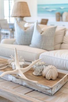 a living room with white furniture and sea shells on the coffee table in front of it