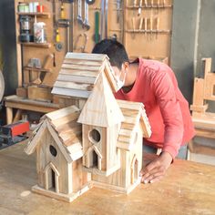 a man in a red shirt working on a wooden birdhouse