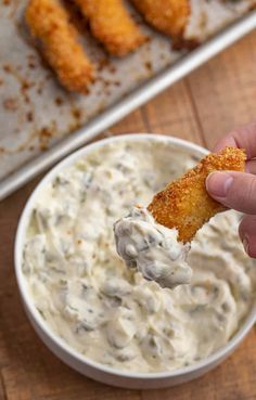 a person dipping something into a bowl of dip with chicken tenders on the side