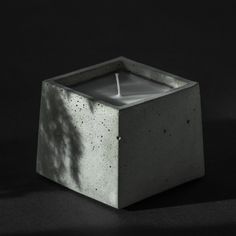 a concrete square candle holder with a lit candle in the center on a black background