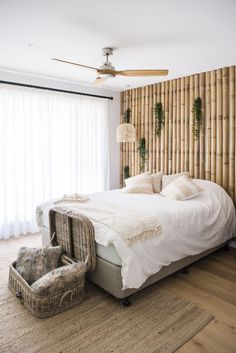 a bed with white linens and pillows in front of a bamboo headboard that has plants on it