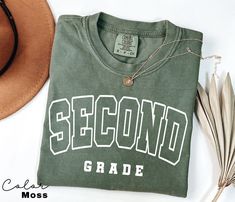 a green shirt with the word second grade on it next to a hat and feathers