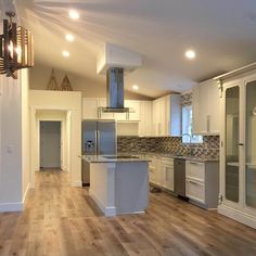 an empty kitchen and living room with hardwood floors in the foreground, white cabinets on either side