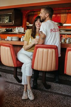 a man and woman sitting at a table in a restaurant with orange booths behind them