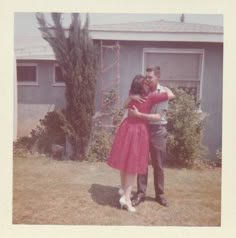 an old photo of a man and woman embracing in front of a house with trees