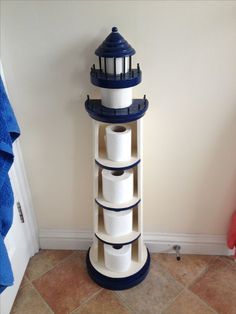 a white and blue lighthouse shaped shelf with toilet paper on it's sides in the corner