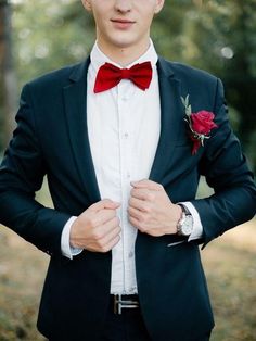 a young man in a blue suit with a red bow tie and rose boutonniere