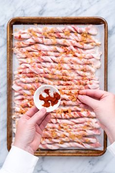 two hands holding a small white bowl filled with red and yellow condiments on top of a baking sheet