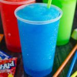 three different colored drinks sitting on top of a table next to candy bars and candies