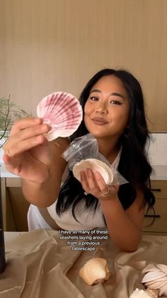 a woman sitting at a table holding up two seashells