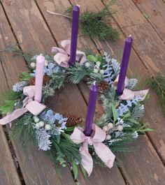 a wreath with purple candles and greenery on a wooden decking area next to pine cones