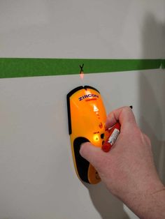 a hand holding a lighter next to an orange and black device on a wall with green stripes