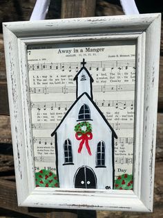 a white frame hanging from a wooden fence with music sheets and holly wreaths on it