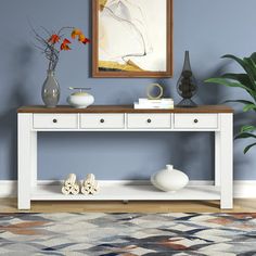 a white console table with three drawers and two vases on the top, in front of a blue wall