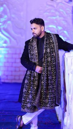 a man standing in front of a white table wearing a black and gold dress coat