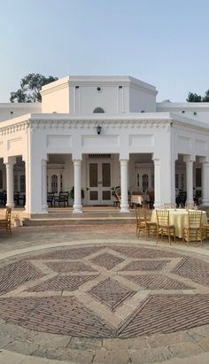 a large white building with tables and chairs in front of it on a circular patio