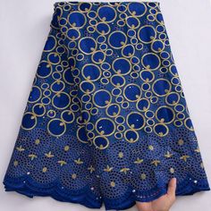 a hand is holding up a blue and gold fabric with golden circles on the side