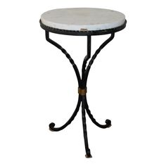 a white marble top table with black iron legs and an ornate design on the base