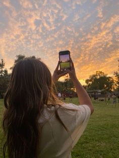 a woman is taking a photo with her cell phone in the park at sunset or dawn