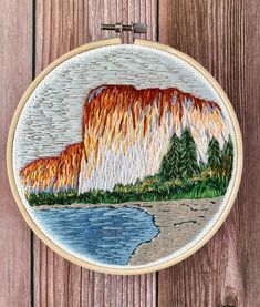 an embroidery project with mountains and trees in the background, on a wooden wall hanging