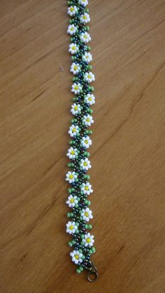 a green and white beaded bracelet with flowers on it sitting on a wooden table