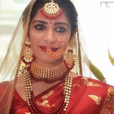 a woman in a red and gold bridal outfit with jewelry on her neck, nose ring and headpiece