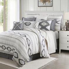 a white bed with black and grey comforter in a bedroom next to a window