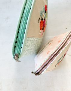 two zippered purses sitting on top of a white table next to each other