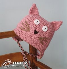 a pink crocheted hat with eyes and ears on top of a wooden chair