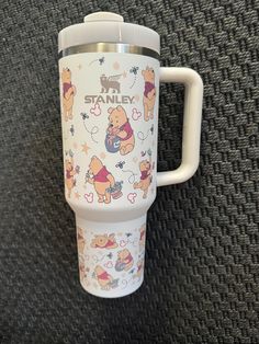 a white travel mug with winnie the pooh characters on it sitting on a carpet