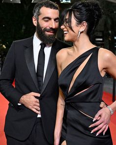 a man and woman standing next to each other on a red carpet with their arms around each other