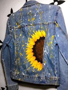 a painted jean jacket with a sunflower on the back and yellow paint splatters all over it