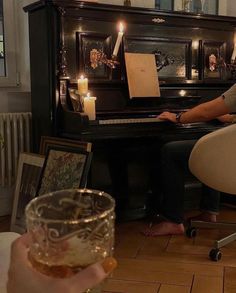 a woman sitting at a piano with a glass of wine in front of her and candles on the table